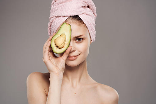Woman with bared shoulders avocado in hands cropped view over gray background. High quality photo