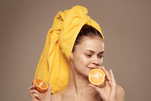 woman with a towel on her head bared shoulders citrus fruits in hands skin care. High quality photo