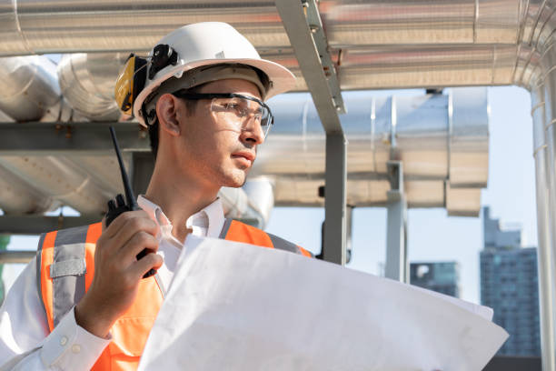 istock Portrait Asia male engineer in protective workwear is performing a conducts system check with use paperwork and walkie talkie at rooftop building 2150088564