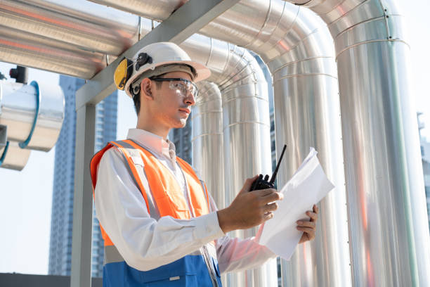 istock Portrait Asia male engineer in protective workwear is performing a conducts system check with use paperwork and walkie talkie at rooftop building 2150088595