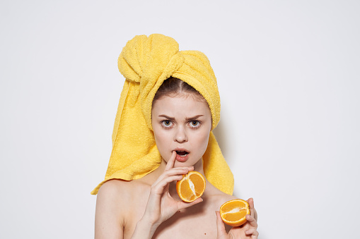 Cheerful woman with a yellow towel on her head bared shoulders oranges in hands health clean skin. High quality photo