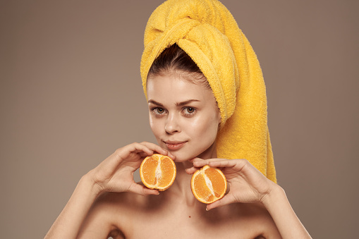 Pretty woman bared shoulders oranges in the hands of a yellow towel on her head. High quality photo