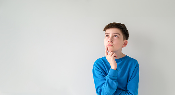 Thoughtful preteen kid boy standing with puzzled serious expression, making choice thinking against white background. Studio shot