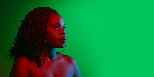 Profile portrait of elegant African woman with curly dark hair, well-kept skin posing on green studio background in neon. Concept of natural beauty, ethnicity, self-care, wellness, positive emotions