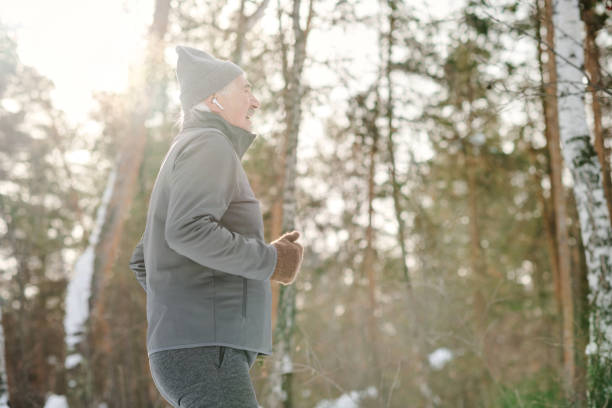Side view of active senior man in sportswear jogging in park on cold winter day, copy space
