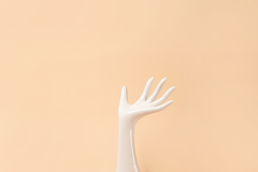 White ceramic statue hand on beige background with copy space