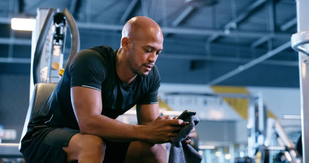 istock Exercise, cellphone and man in gym, wellness and relaxing with digital app, connection and social media. Person, athlete and guy in health center, relax and online game with goals and check progress 2150092690