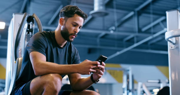 Exercise, smartphone and man in gym, typing and contact with email, check training schedule and online fitness news. Person, athlete and guy in wellness center, relax and cellphone with workout goals