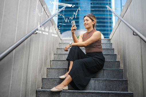 The image depicts an Asian businesswoman using AI smartphones to analyze financial data and create charts. It illustrates the concept of financial technology.