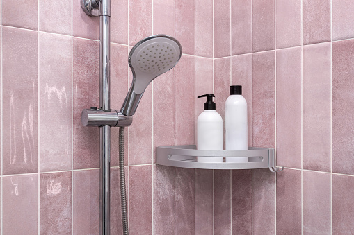 Bottles for shampoo and gel in the bathroom against the backdrop of pink tiles and shower.