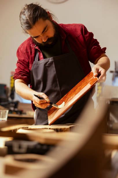 istock Cabinetmaker in carpentry shop lacquering wooden board 2150098126