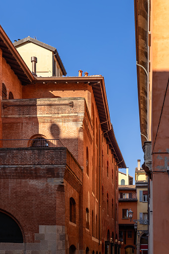 The sun casts a gentle shadow on the terracotta façades of Bologna, creating a harmonious interplay of light and texture in this serene urban passage