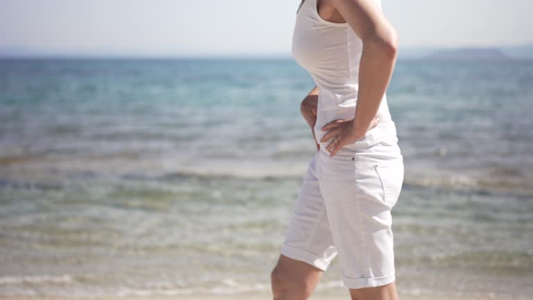Mature woman suffering from abdominal pain while walking on the beach