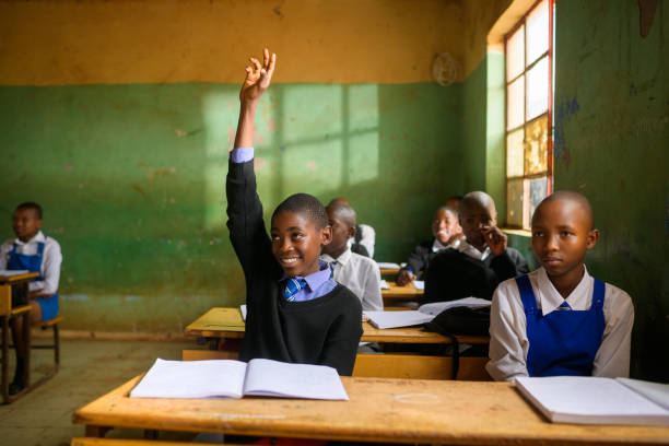 African Schoolboy in rural classroom with other students.  He looks keen to learn and be educated.  He has his hand raised.  Malealea, Lesotho.