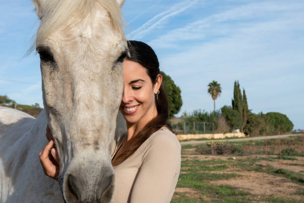 Woman embracing white horse with eyes closed.