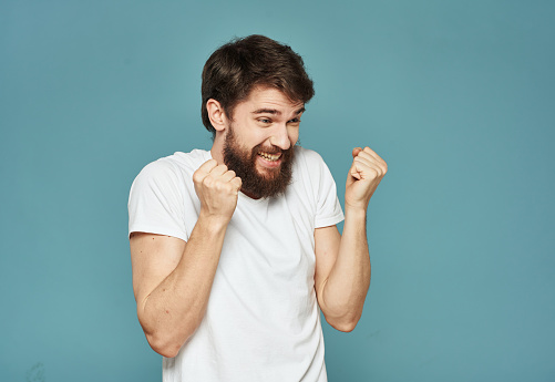 A successful man in a white T-shirt clenched his hands into a fist on a blue background. High quality photo