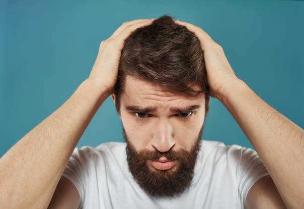 A man on a blue background is touching his head with his hands. High quality photo