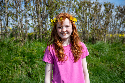 Portrait of a smiling young girl in a pink t-shirt standing outdoors in the sunshine