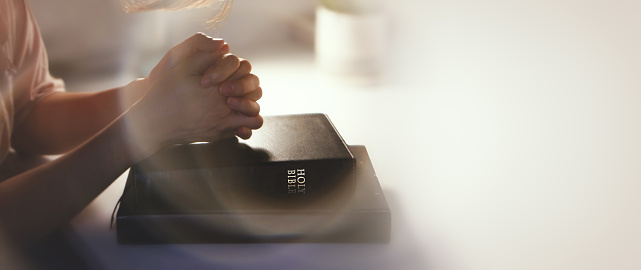 Christian background with hands placed together on a holy bible at a desk, meditating, praying and worshiping