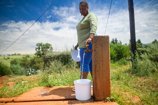 Woman collecting water in a bucket at an outdoor community water tap faucet water point in a rural setting, Malealea, Lesotho.