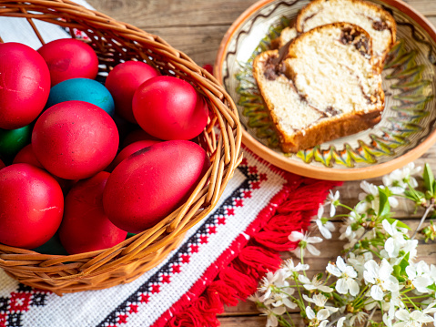 red easter eggs in a wicker basket on a wooden background with apple flowers aside
