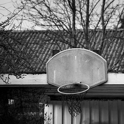 Black and white basketball net hoop mounted on wood in poor neighborhood, showing social division.