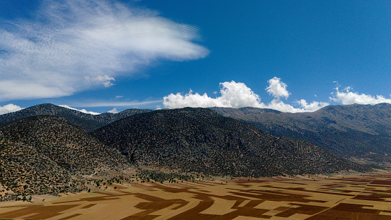 Dry desert foreground with desert plants to hills in middleground rolling toward distant mountain range of Eastern Sierra Nevadas of California, USA