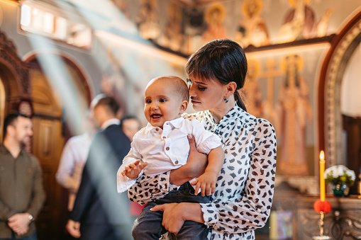 Young mother holding her baby boy during christening in an Orthodox church.