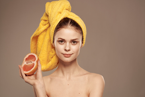 Pretty woman with towel on her head clean skin bared shoulders citrus fruit in hands. High quality photo