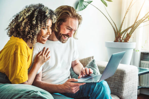 istock Multiracial young couple watching computer laptop sitting on the sofa at home - Happy diverse husband and wife using pc online services - Technology life style concept 2150116072