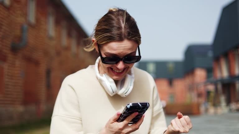 Woman saying no way and laughing while looking at screen of phone on street