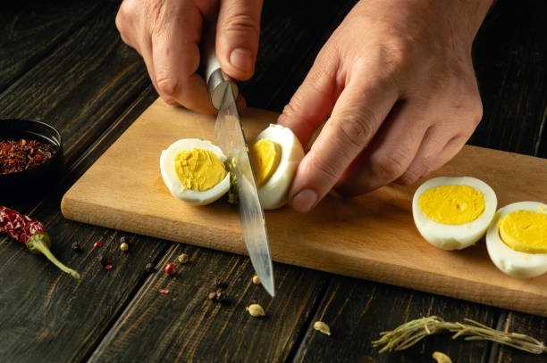 istock Close-up of a man hands with a knife slicing a boiled egg on a kitchen cutting board before preparing a breakfast dish at home 2150117738