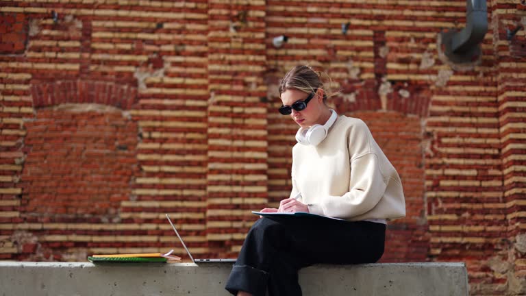 Thoughtful caucasian female writing compendium in personal notebook outdoors