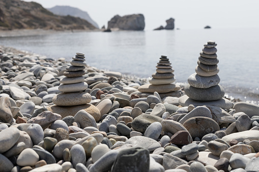 Foreground of balanced stone cairns on a pebble beach with the famous Aphrodite's Rock in the background, Cyprus.