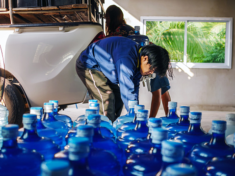 Workers lift drinking water 
clear and clean in blue plastic gallon into the back of a transport truck purified drinking water inside the production line to prepare for sale. Water drink factory, small business