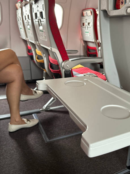 istock Image of airplane cabin interior, empty fold down table, row of empty plane seats, unrecognisable woman with leg crossed over knee, rear view, focus on foreground 2150121241