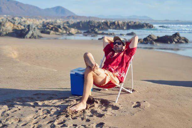 mature man sitting alone with hands behind head relaxed enjoying beach and nature