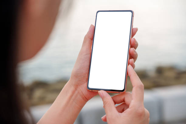 Over-the-shoulder view of an Asian woman using a smartphone with a blank screen while walking by the beach.