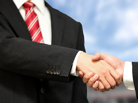 An Asian businessman wearing a suit is shaking hands with a businessman outdoors