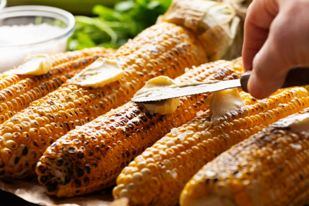 istock Grilled sweetcorn cobs on the table being seasoned with butter closeup low angle view 2150129517