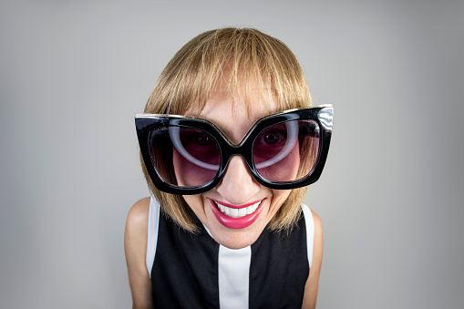 A fisheye image of a middle aged woman with short blond hair wearing gigantic sunglasses.