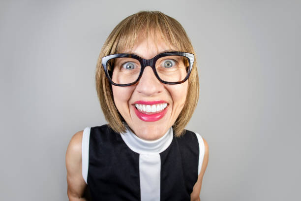 A fisheye image of a happy older woman wearing black rimmed glasses.