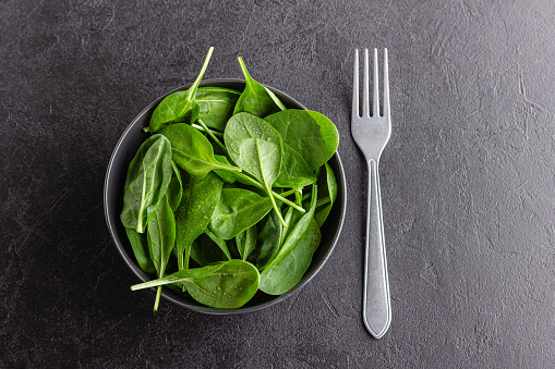 Fresh green spinach leaves in the bowl. Natural vegetarian food on black table.