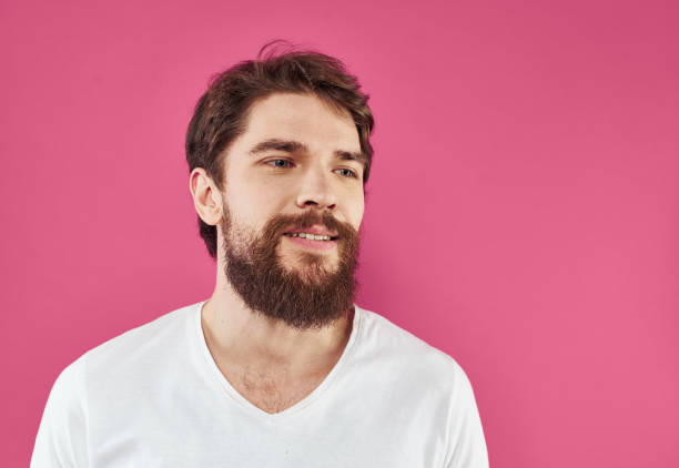 istock Happy guy in a white T-shirt on a pink background with a thick beard is gesturing with his hands 2150132104