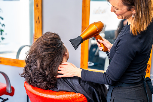 Rear view of a hairstylist drying the curly hair of a client in the salon