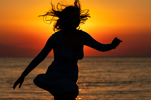 Silhouette of carefree woman on the beach at sunset