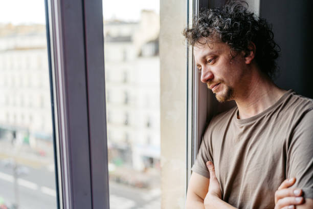 Depressed young man looking out the window and contemplating life in Paris in France.