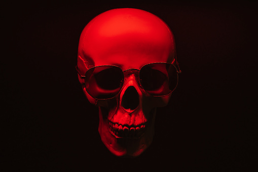 human skull wearing sunglasses in red light on a black background