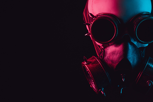 human skull in steampunk glasses and a gas mask with pink and blue light on a black background