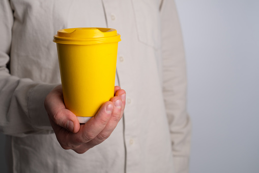 Yellow craft paper cup for coffee in a man's hand on a white background. Hot drink. Disposable paper cup close up. Empty space for text, layout. Coffee to go concept